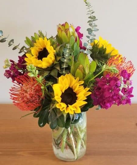 A mix of farm flowers in bright colors arranged in a mason jar.