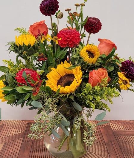 Sunflowers, roses and helenium in classic Autumn colors. Local dahlias included when in season. Dahlias will be substituted with a comparable product in late Fall.